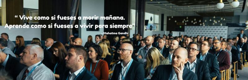A group of people attending a business seminar and the quote "Vive como si fueses a morir manana. Aprende como si fueses a vivir para siempre" - Attribuido a Mahatma Gandhi