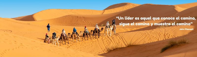 Una caravana recorriendo el desierto con la cita: «Un líder es aquel que conoce el camino, sigue el camino y muestra el camino» - Atribuido a John C. Maxwell.