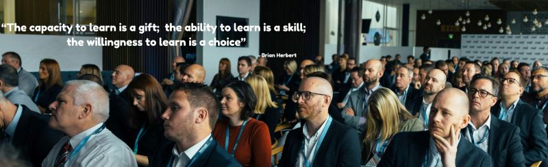 A group of people attending a business seminar and the quote "The capacity to learn is a gift; the ability to learn is a skill; the willingness to learn is a choice" - Attributed to Brian Herbert
